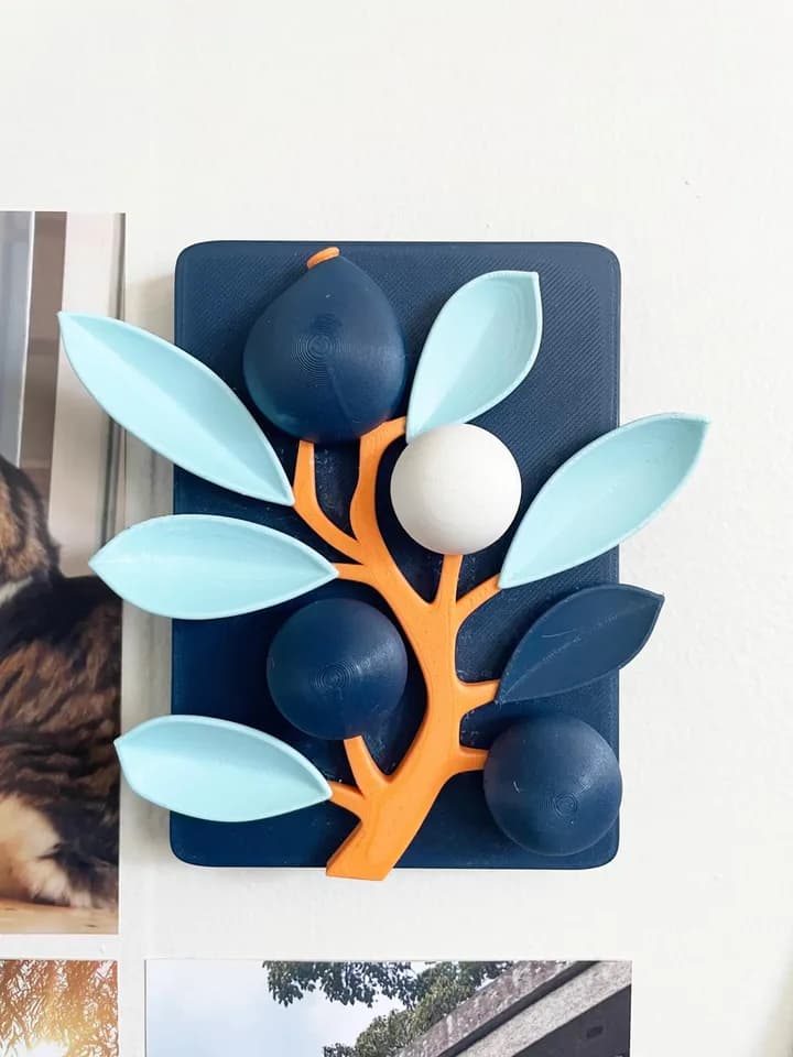 Botanical wall relief with an orange branch and pale blue leaves on a navy panel