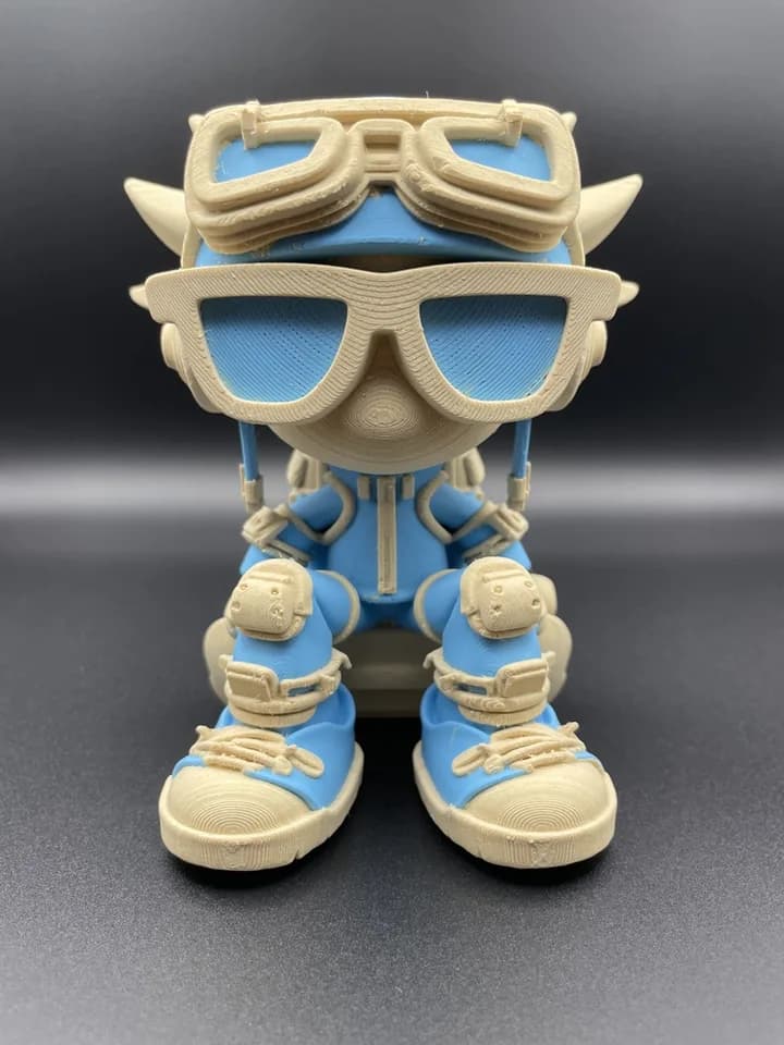Blue and cream character figurine wearing oversized sunglasses, goggles, and boots