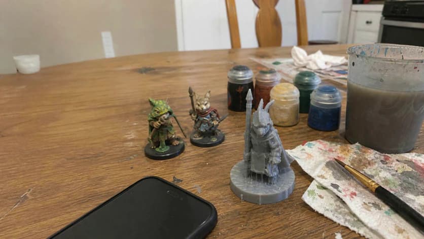 Painted and unpainted miniatures beside brushes and paint pots on a worktable